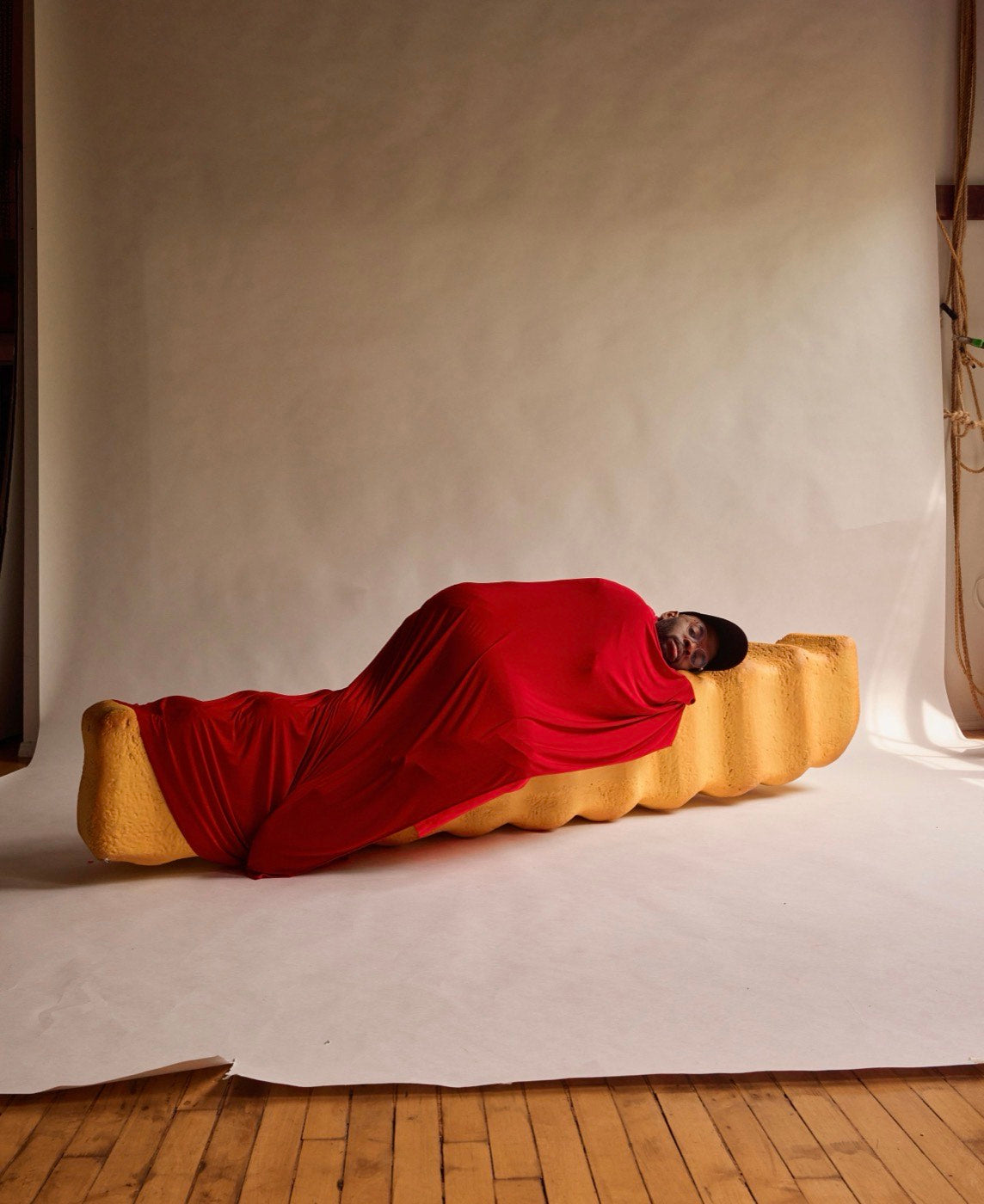 Paul Octavious lying on a giant foam french fry in the studio, wrapped in red cloth